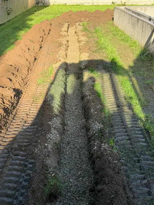 A stone-filled drainage trench with the digger's shadow across it